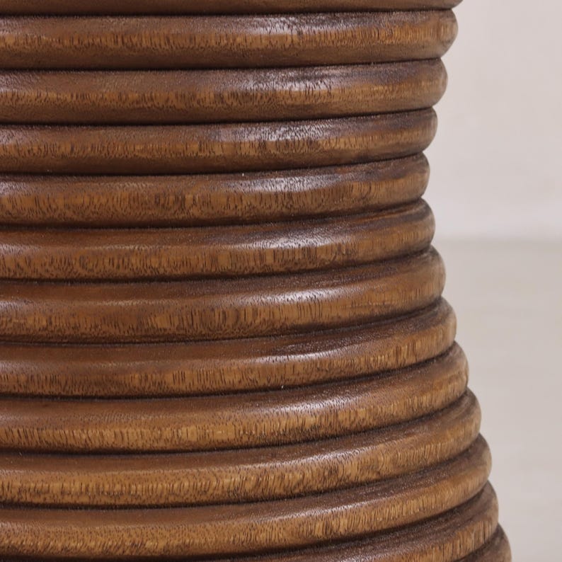 May include: Close-up of a brown wooden table base with a unique, layered design. The base is made of multiple rings of wood stacked on top of each other, creating a textured and visually interesting surface.