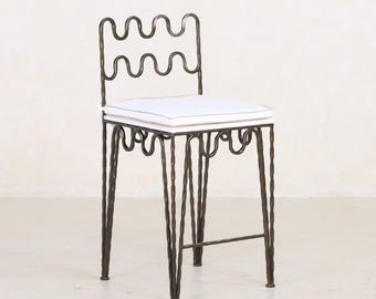 May include: A white cushioned bar stool with a black metal frame. The frame is made of twisted metal and has a wavy design.