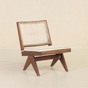 May include: A wooden chair with a woven cane back and a white cushion. The chair has a dark brown finish and a unique angled design.