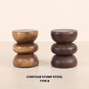 May include: Two wooden contour stump stools, one brown and one dark brown, each with three stacked rounded tiers. The stools are made of solid wood and have a natural finish. "Contour Stump Stool Type B" is written below the stools.
