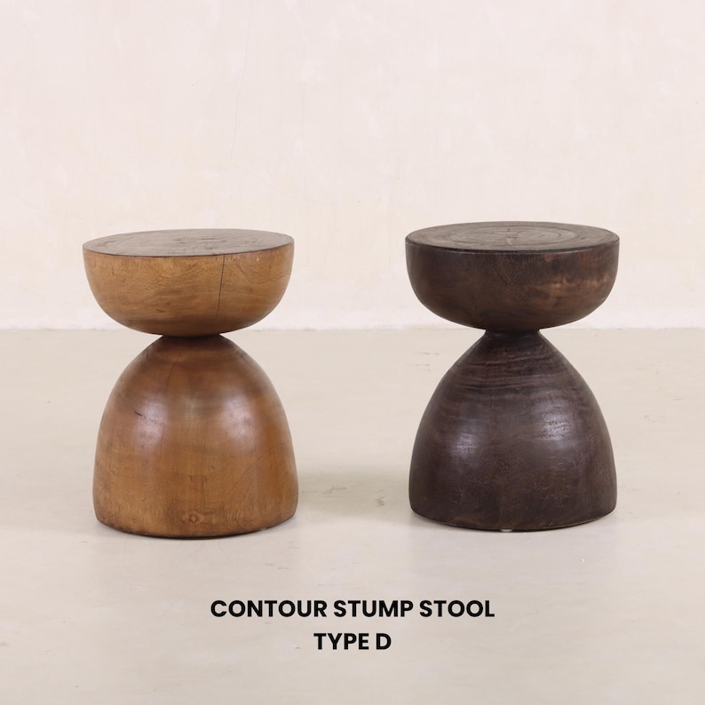 May include: Two wooden contour stump stools, one in a light brown wood and the other in a dark brown wood. The stools are shaped like an hourglass with a round top and a rounded base. The text "CONTOUR STUMP STOOL TYPE D" is printed below the stools.