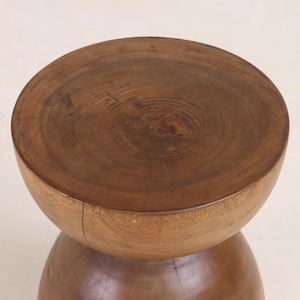 May include: A wooden stool with a round, brown top and a rounded, hourglass-shaped base.