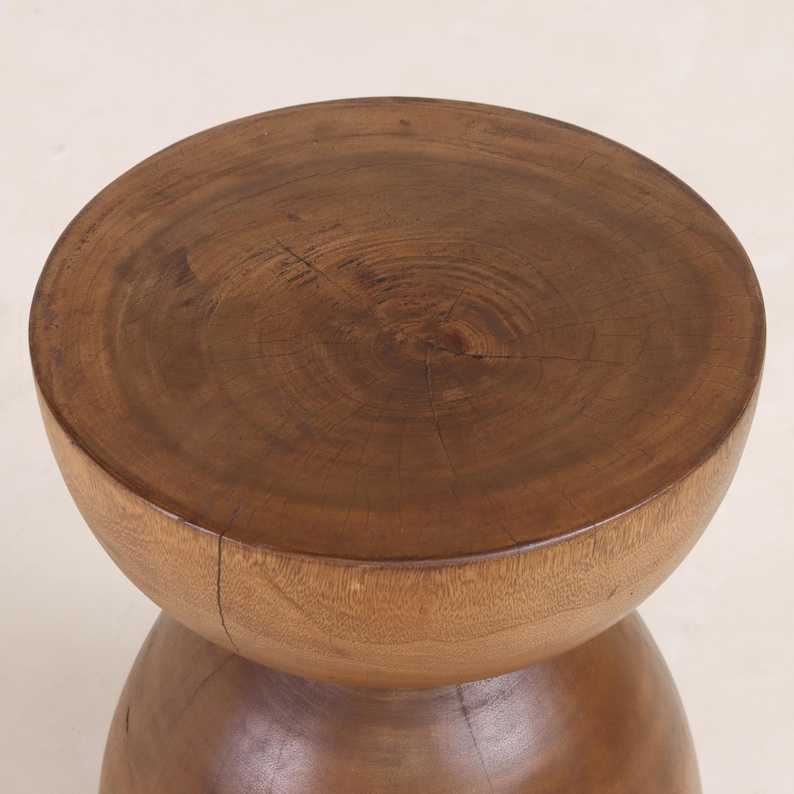 May include: A wooden stool with a round, brown top and a rounded, hourglass-shaped base.