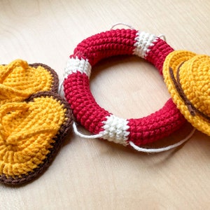 May include: Crocheted summer themed set with a red and white life preserver, a yellow hat with a brown band, and two yellow flip flops with brown trim.