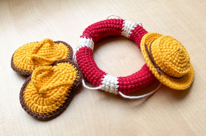 May include: Crocheted summer themed set with a red and white life preserver, a yellow hat with a brown band, and two yellow flip flops with brown trim.