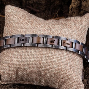 May include: A silver and brown bracelet with engraved initials "A♥S" and "HHH" and the date "10.08.24".