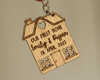 May include: A wooden house-shaped keychain with the text "Our First Home Emily & Regan 26 April 2023" engraved on it.