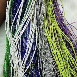May include: A collection of colorful beaded necklaces in various shades of green, blue, white, and gray. The necklaces are made of small, round beads and are strung together in a long, continuous strand.