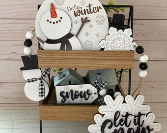 May include: A two-tiered black metal stand with wooden shelves, decorated with winter-themed wooden ornaments. The top shelf features a snowman with the words "hello winter" and a snowflake. The bottom shelf has a snowman, a sign that says "snow", and a snowflake with the words "let it snow".