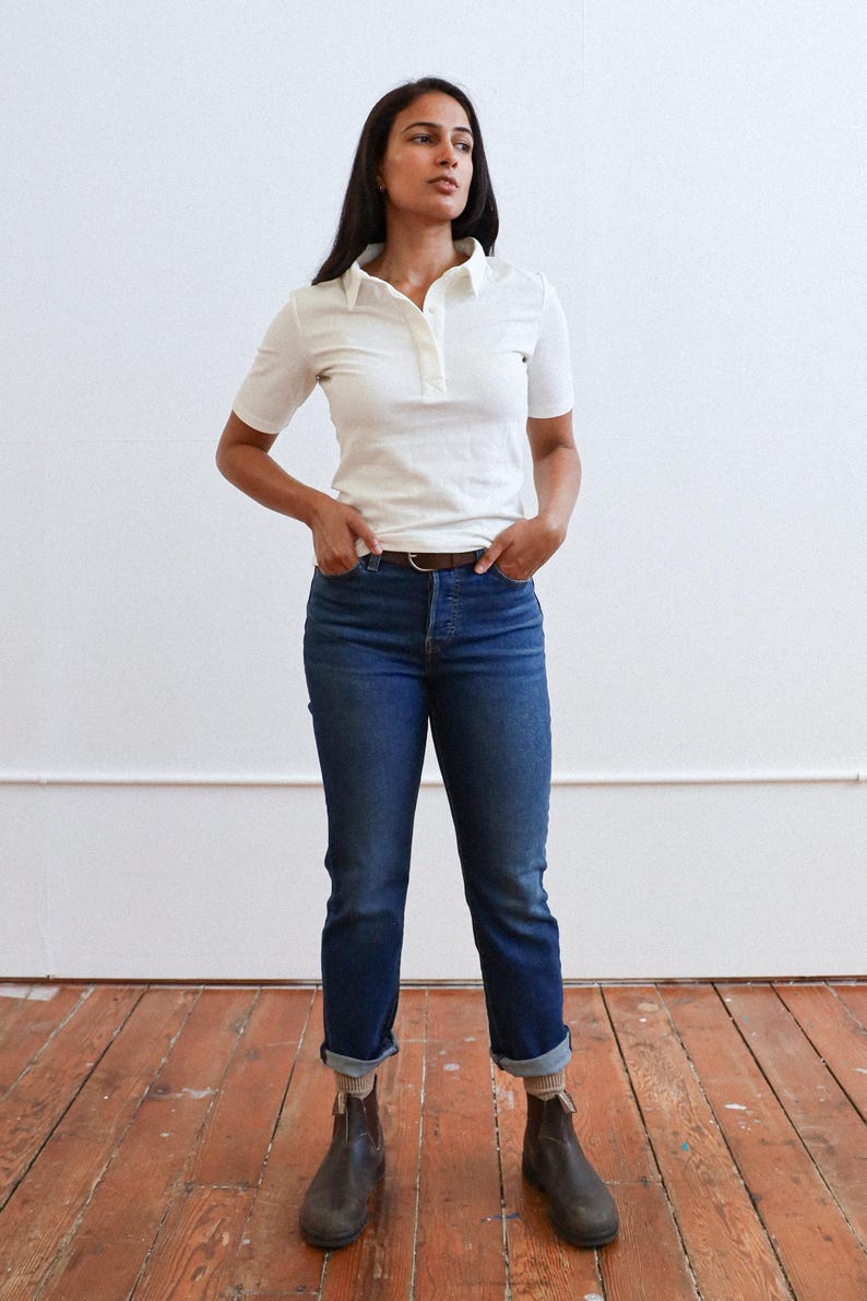 Pode incluir: Uma mulher vestindo uma camisa branca de colarinho, cinto marrom e jeans azul. Ela est&aacute; usando botas de tornozelo marrons.