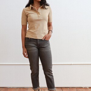 Pode incluir: Uma mulher vestindo uma camisa bege de colarinho e cal&ccedil;as jeans cinza escuras com botas de cano curto marrons.