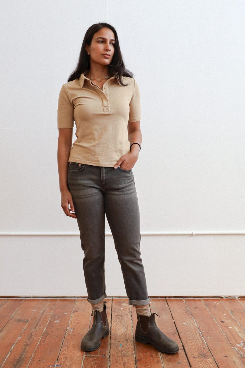 Pode incluir: Uma mulher vestindo uma camisa bege de colarinho e cal&ccedil;as jeans cinza escuras com botas de cano curto marrons.