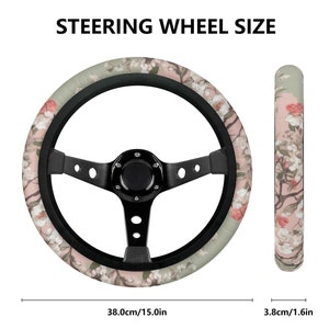 May include: A black steering wheel cover with a floral print featuring pink and white flowers on a light green background. The steering wheel is 15 inches in diameter and the cover is 1.6 inches wide.