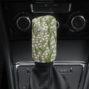 May include: A white and green patterned gear shift knob with a white flower design. The knob is made of fabric and has a stitched seam around the top.