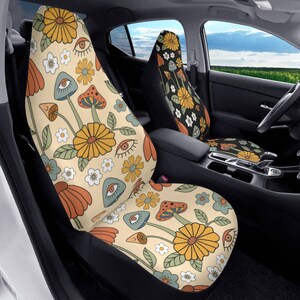 May include: A pair of car seat covers featuring a cream-colored background with a repeating pattern of yellow daisies, orange flowers, blue and orange mushrooms, and stylized eyes with green leaves scattered throughout the design.