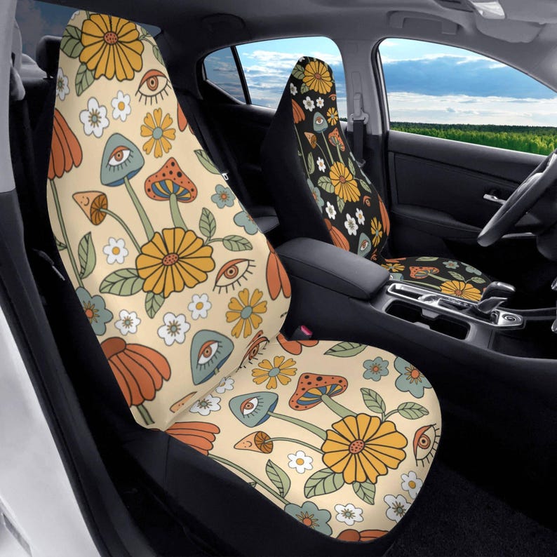 May include: A pair of car seat covers featuring a cream-colored background with a repeating pattern of yellow daisies, orange flowers, blue and orange mushrooms, and stylized eyes with green leaves scattered throughout the design.
