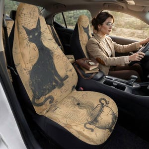 May include: A tan car seat cover featuring a black cat illustration and a line drawing of a steaming cauldron. The background is printed with faint, cursive script text. The cover is fitted over the front seat of a vehicle with a matching headrest.