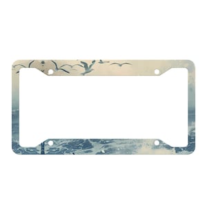 Puede incluir: Marco de matrícula con una escena costera. La parte superior representa gaviotas en vuelo contra un cielo beige claro. La mitad inferior muestra olas del océano en tonos azules y blancos. El marco tiene cuatro orificios de montaje.