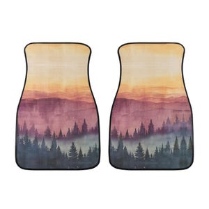 May include: A set of two car floor mats with a watercolor design of a misty mountain range with a sunset sky. The mats are a light brown color with a dark brown border.
