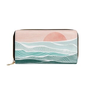 Puede incluir: Una cartera negra con cremallera con un dise&ntilde;o abstracto colorido de una puesta de sol sobre el oc&eacute;ano. El dise&ntilde;o presenta un sol rosa, olas blancas y agua verde y azul.
