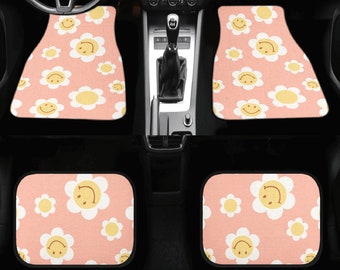 May include: Four car floor mats featuring a repeating pattern of smiling daisy flowers. The mats are light pink with white and yellow flowers. Designed to fit in a car, they offer a cheerful interior upgrade.