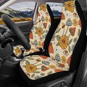 May include: A pair of car seat covers featuring a cream-colored background with a repeating pattern of orange and yellow flowers, green leaves, small white blossoms, various mushrooms in shades of blue and orange, and stylized open eyes.
