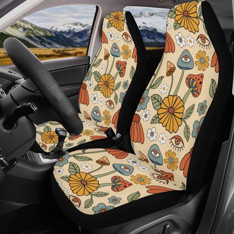 May include: A pair of car seat covers featuring a cream-colored background with a repeating pattern of orange and yellow flowers, green leaves, small white blossoms, various mushrooms in shades of blue and orange, and stylized open eyes.