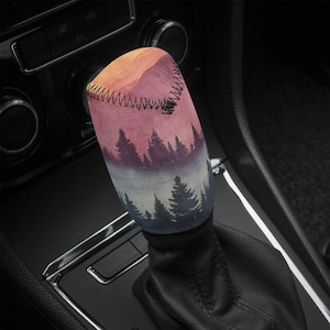 May include: A colourful gear shift knob with a forest scene design. The knob features a sunset gradient with a silhouette of trees and a misty background.