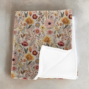 May include: A soft, plush baby blanket with a floral print featuring a variety of flowers in shades of yellow, pink, and red. The blanket has a white fleece backing.