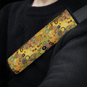 May include: A yellow, blue and green patterned car seatbelt cover with a swirling design. The cover is made of fabric and is designed to protect the seatbelt from wear and tear.