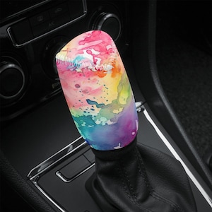 May include: A colourful watercolor-style gear shift knob cover with pink, orange, yellow, green, and blue splatter paint design.