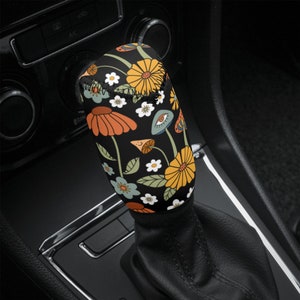 May include: A black gear stick knob with a colourful floral pattern. The pattern includes yellow, orange, green, blue and white flowers and mushrooms.