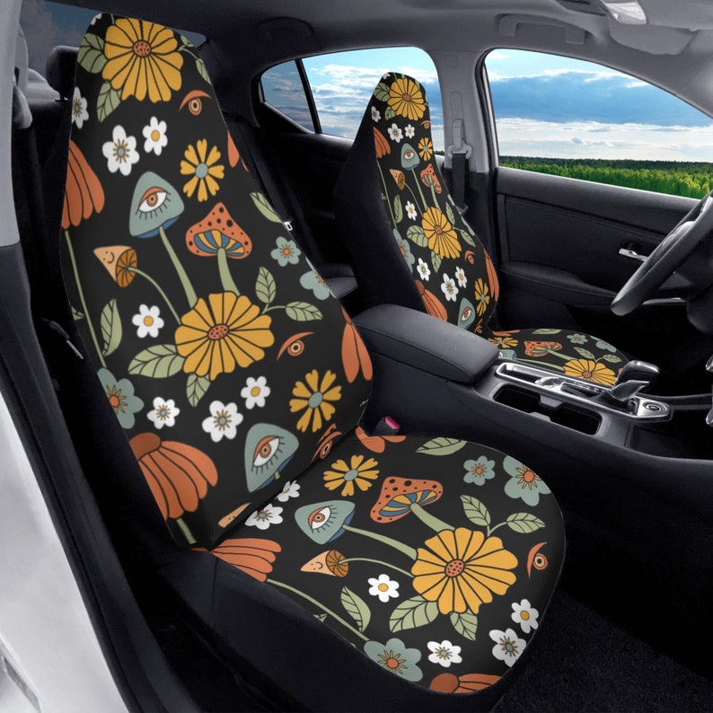 May include: A pair of car seat covers featuring a black background with a repeating pattern of yellow flowers, white daisies, orange petals, green leaves, and light blue mushrooms with human eyes integrated into the mushroom caps.