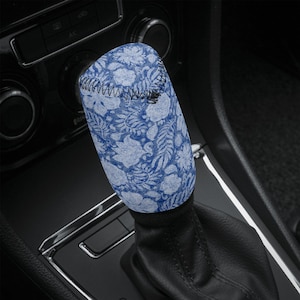 May include: A blue and white floral pattern gear stick cover. The cover is made of a soft material and is stitched with black thread. The gear stick is in a car interior.