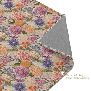 Puede incluir: Una alfombra beige con un patrón floral con flores rosas, moradas, naranjas y amarillas. La alfombra tiene un diseño de bordado falso y un respaldo gris.