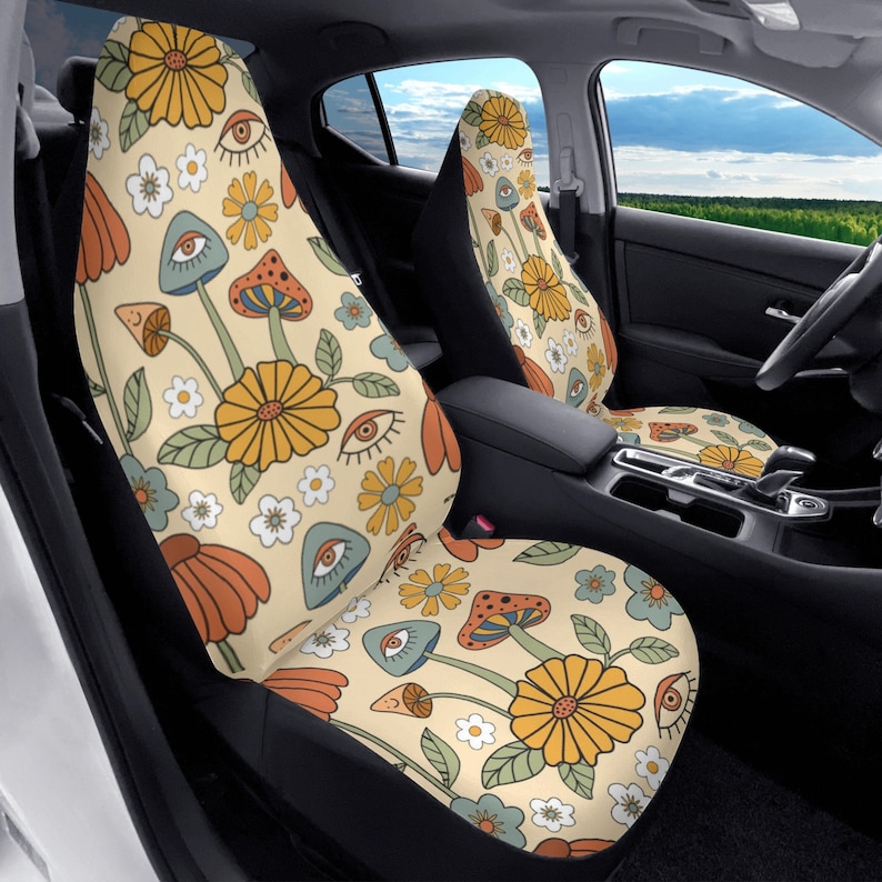 May include: A pair of car seat covers featuring a cream-colored background with a repeating pattern of yellow flowers, orange mushrooms, blue mushrooms with eyes, and small white flowers. The design covers the front and seat areas of the car seats.