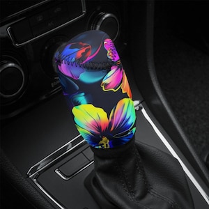May include: A black shift knob cover with a colourful floral pattern in yellow, pink, purple, and blue. The cover is made of a stretchy material and is designed to fit over a car's gear shift.