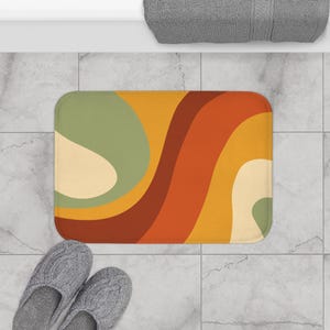 Peut inclure: Un tapis de bain avec un motif abstrait rétro composé de lignes ondulées dans des tons d'orange, de brun, de jaune et de vert.
