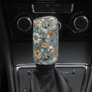 May include: A blue and green gear shift knob with a floral and bee pattern. The knob is made of fabric and has a stitched seam around the top.