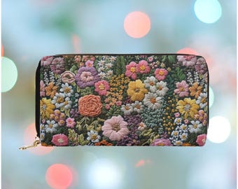 Op de afbeelding: Een geborduurde portemonnee met een zwarte rits en een goudkleurige trekker. De portemonnee heeft een gedetailleerd patroon van kleurrijke bloemen in tinten roze, geel, oranje en wit tegen een donkergroene achtergrond.