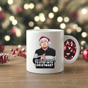 May include: White ceramic mug with a cartoon image of a man in a Santa hat. The mug features the text "ARE YOU ASKING ME TO STEP INTO CHRISTMAS?". The mug has a white handle and is set against a festive background.