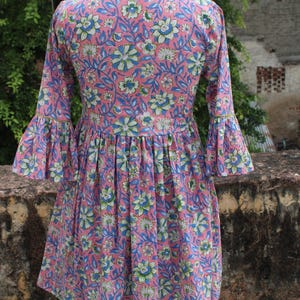 May include: A pink and blue floral print dress with a gathered waist and bell sleeves. The dress has a high neckline and a fitted bodice.