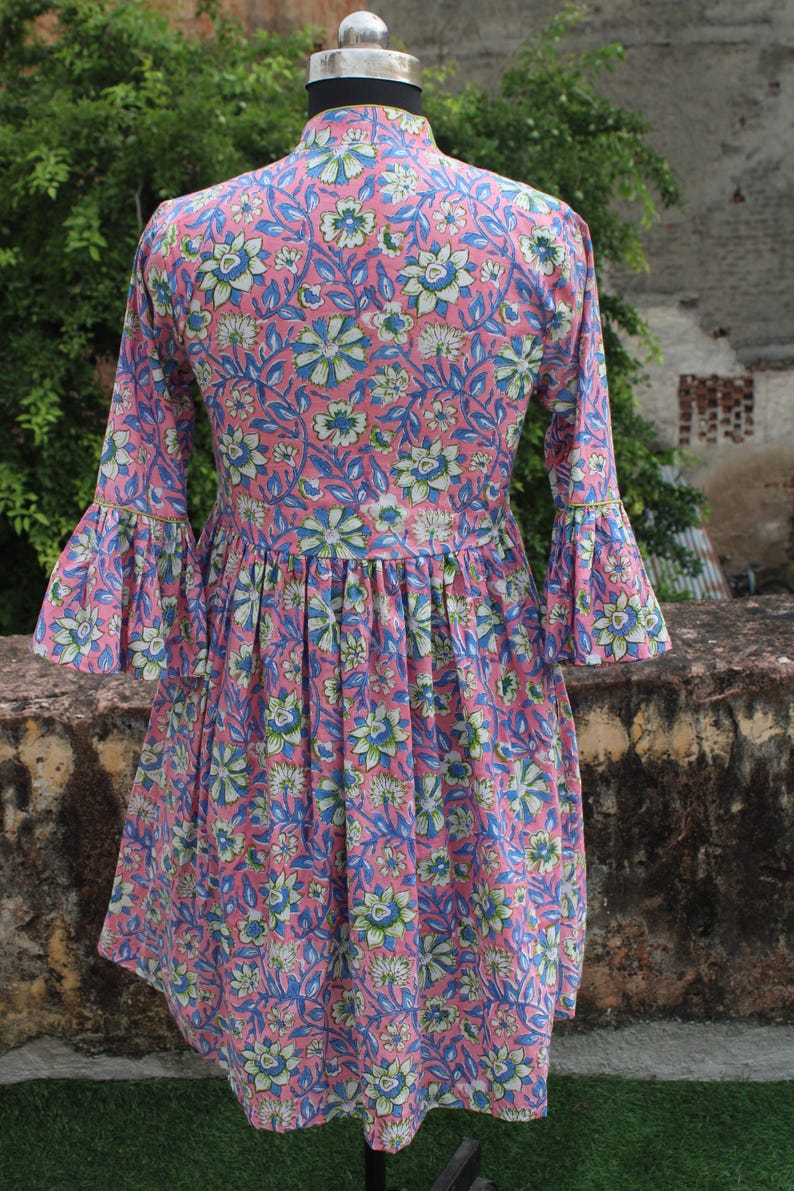 May include: A pink and blue floral print dress with a gathered waist and bell sleeves. The dress has a high neckline and a fitted bodice.