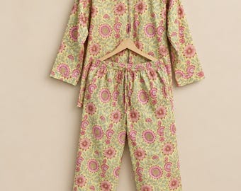 May include: A long-sleeved button-down shirt and matching drawstring pyjama trousers featuring a light yellow base with a repeating pink and green floral pattern, accompanied by a small rectangular envelope-style pouch in the same fabric.