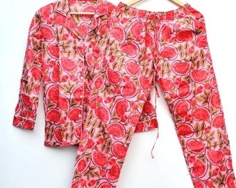 Può includere: Un set pigiama a due pezzi composto da una camicia a maniche lunghe con bottoni e colletto e pantaloni lunghi abbinati. Il set presenta uno sfondo rosa chiaro con un motivo ripetuto di fiori rossi e foglie marroni su tutto il tessuto.