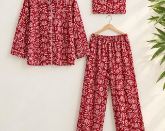 以下が含まれることがあります： 深い赤色に白い花柄が施された3ピースのパジャマセット。襟付きの長袖ボタンダウンシャツ、伸縮性のあるウエストバンドを備えたワイドレッグパンツ、そしてお揃いの生地で作られた長方形のヘッドバンドが含まれています。
