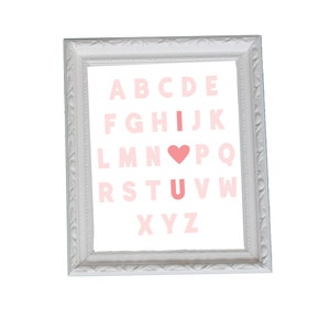 May include: A white framed print with a pink alphabet and a pink heart replacing the letter "O" in the word "LOVE".