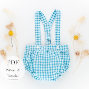 Puede incluir: Un pelele de bebé a cuadros azules y blancos, con tirantes y botones blancos. El texto "PDF Pattern & Tutorial 1 to 36 months" es visible. Flores secas y una flor amarilla están dispuestas alrededor del pelele.
