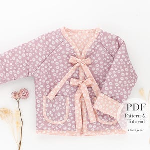 Peut inclure: Veste violet clair à pois blancs et bordures pêche. La veste a deux poches et est nouée avec des rubans pêche. Les manches ont des poignets pêche. Le texte "PDF Pattern & Tutorial 1 to 12 yrs" est inclus.