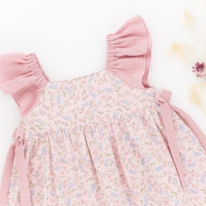 K&ouml;nnte beinhalten: Ein rosa Blumenkleid mit R&uuml;schen&auml;rmeln und Bindeb&auml;ndern. Das Kleid ist aus einem weichen, leichten Stoff gefertigt und hat einen zarten Blumendruck.